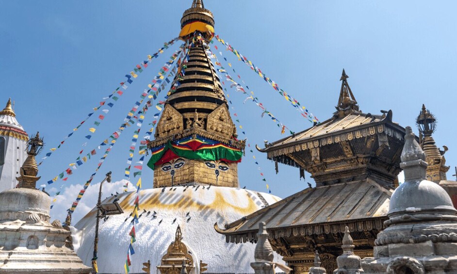 A large stupa with colorful prayer flags, traditional Tibetan architecture, and a clear blue sky. 2