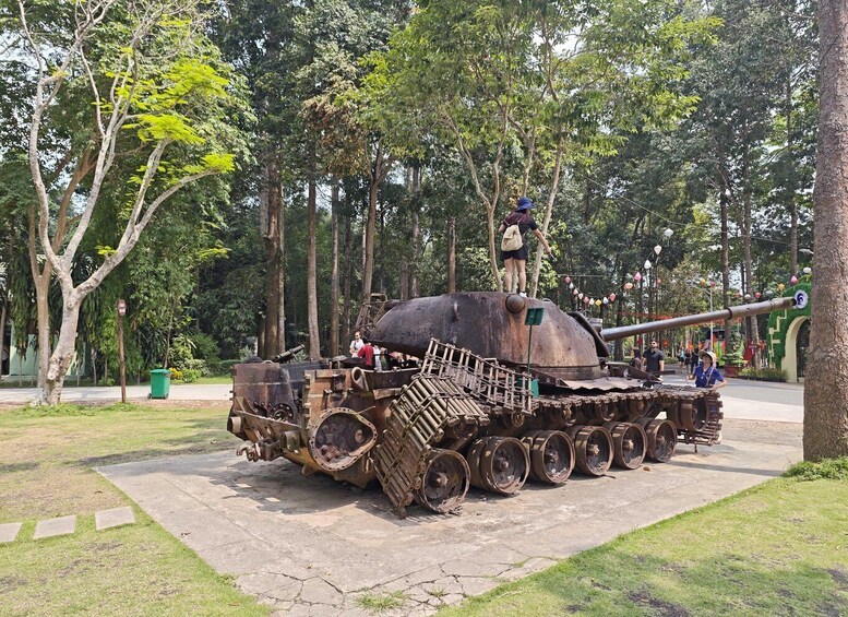 A large, rusted tank on display in a park with trees and a paved walkway. 4