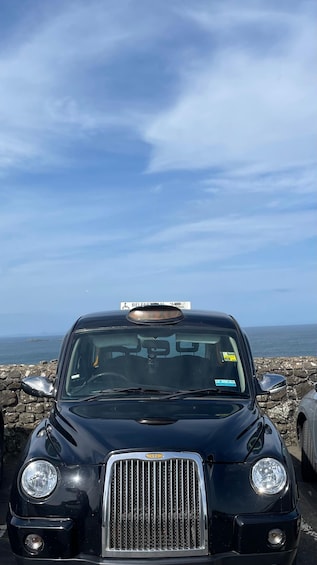 A black luxury car parked on a rocky seaside with a clear sky in the background. 1