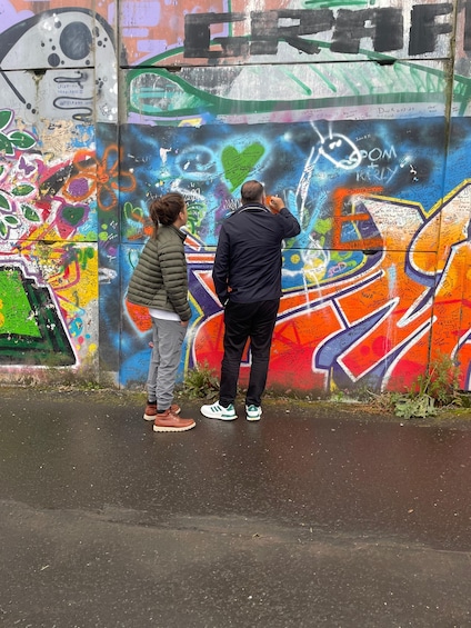 Two people standing in front of a colorful graffiti-covered wall. 2