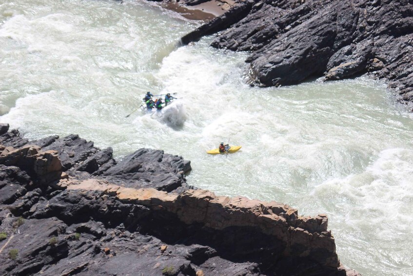 A river with white water rapids, a group of people in a raft, and a single kayaker. 3