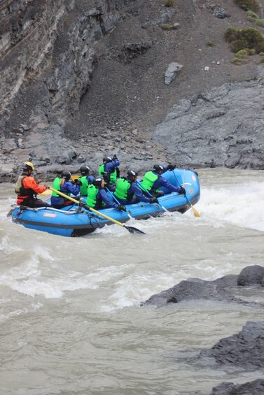 A group of people in a blue raft navigating a river with rapids. 2