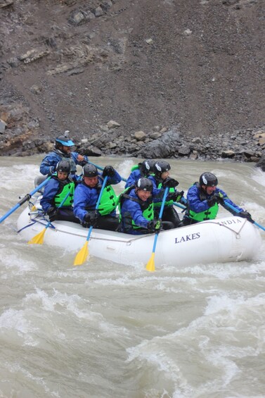 A group of people in a white inflatable raft labeled "LAKES" navigating a river. 5