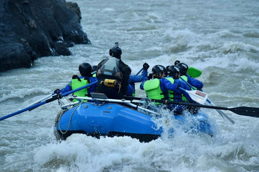 A group of people in a blue raft navigating rough waters. 1