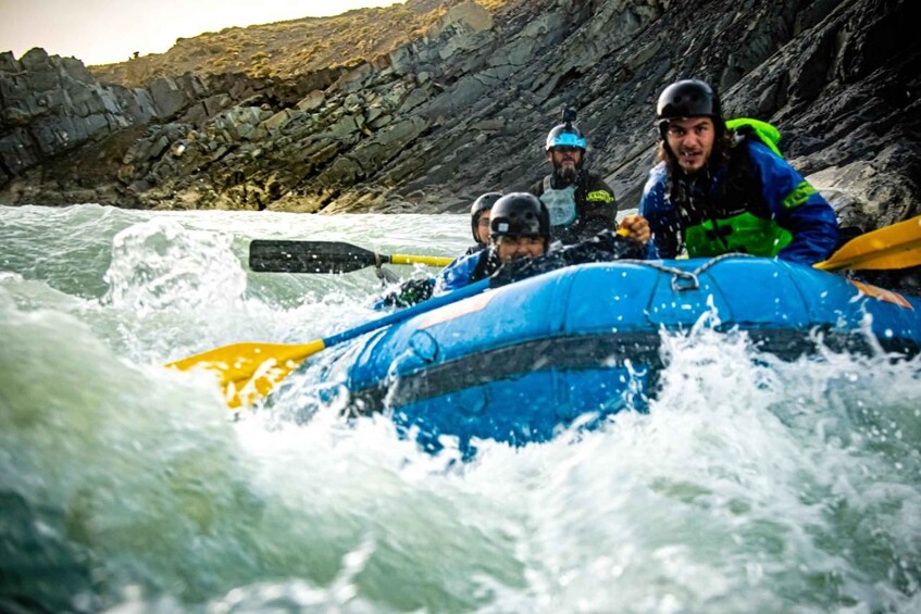 A group of people in a blue raft navigating rough waters. 4