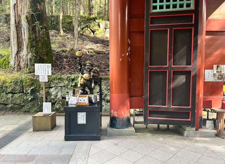 A shrine with a red and black door, a statue, and a stone wall. 4