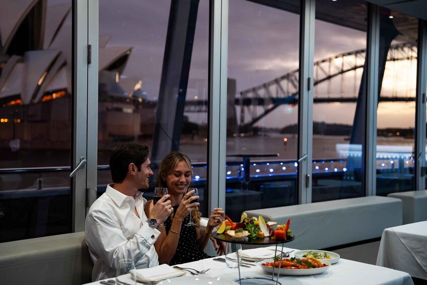A couple dining at a table with a view of a bridge and a building in the background. 1