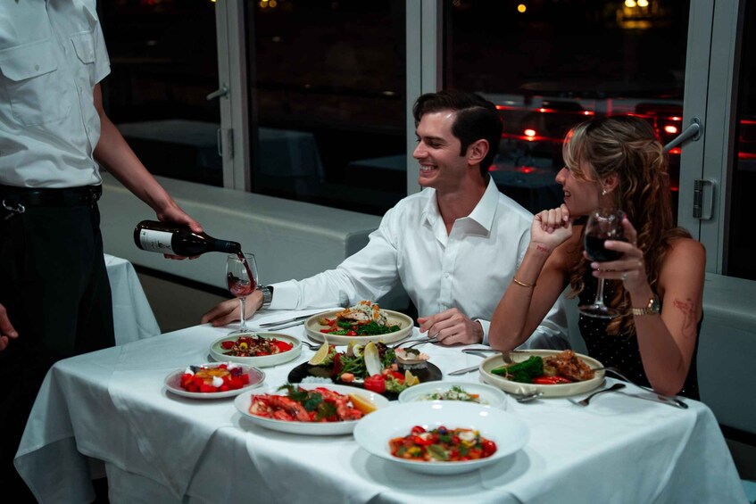 A man pouring wine into a glass, a woman holding a wine glass, and various dishes on a table. 2