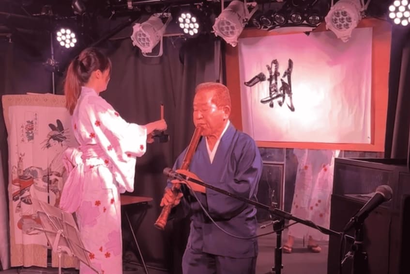 A person playing a traditional string instrument on stage with a microphone. 3