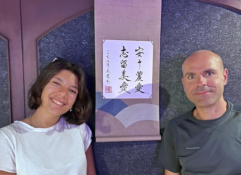 Two people standing in front of a wall with a sign in Japanese. 5