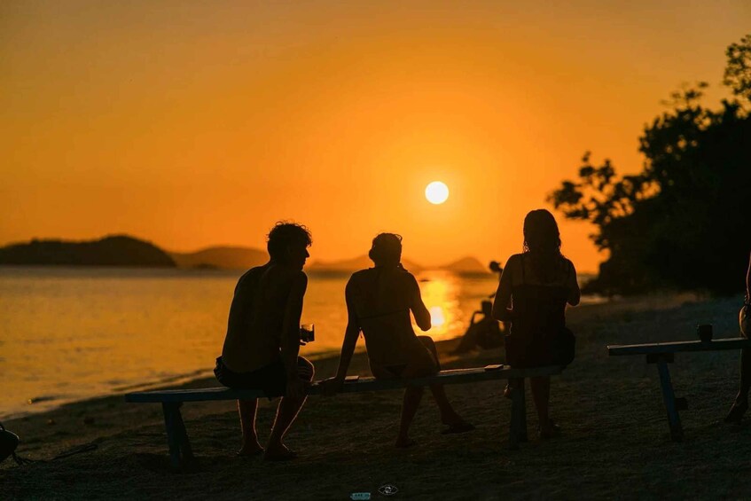 Three people sitting on a bench at sunset by the water. 2