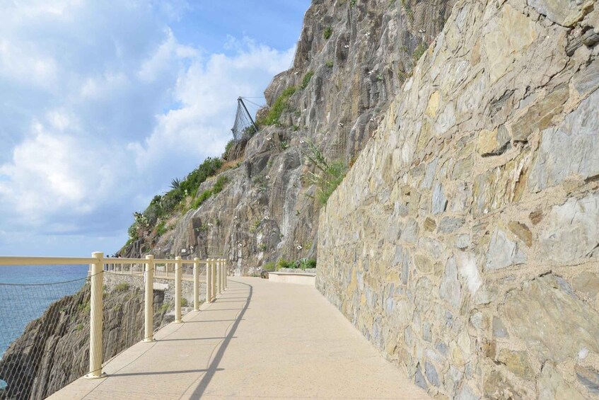 A coastal walkway with a stone wall and a netted structure on a cliff. 5