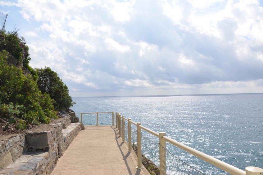 A coastal walkway with a railing, leading to the sea under a partly cloudy sky. 3
