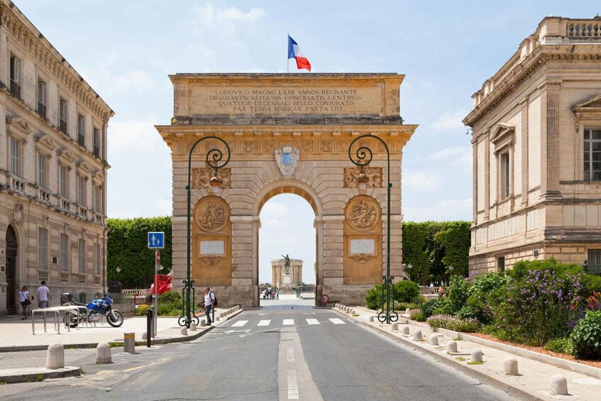 The Arc de Triomphe in Paris, with the French flag on top, surrounded by classical architecture and greenery. 1