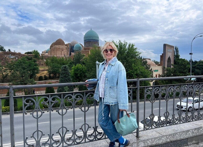 A person standing on a bridge with a cityscape in the background, including domed buildings and a tower. 3