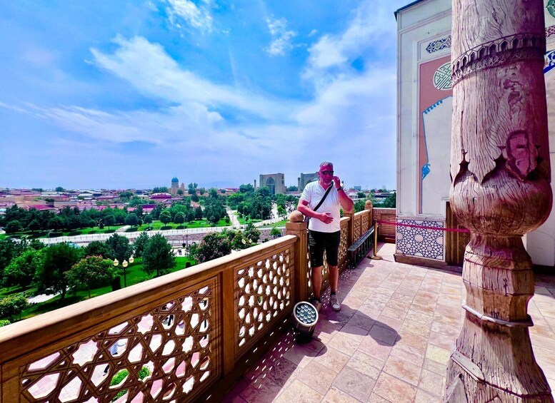 A man standing on a balcony with a view of a cityscape and greenery. 2