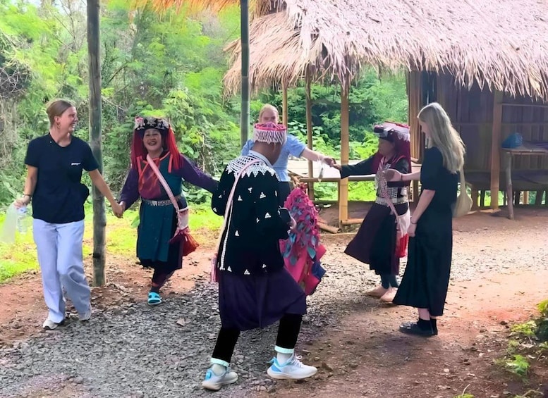 A group of people in traditional attire walking on a dirt path surrounded by greenery and a thatched-roof structure. 4