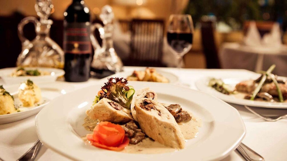 A formal dining setting with plates of food, wine glasses, and a bottle of wine. 4