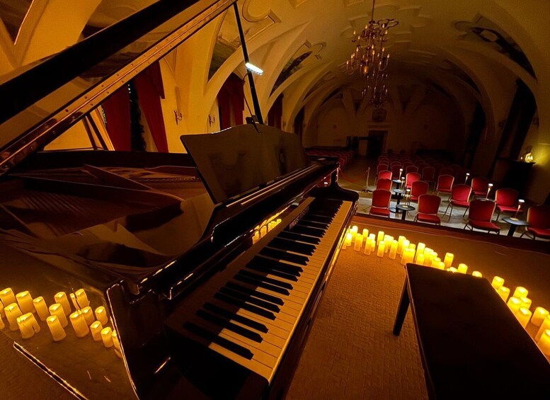 A grand piano in a dimly lit room with red chairs and candles. 3