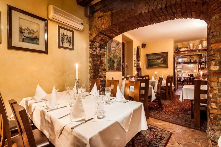 A dining area with a stone archway, white tablecloths, and framed artwork on the walls. 1