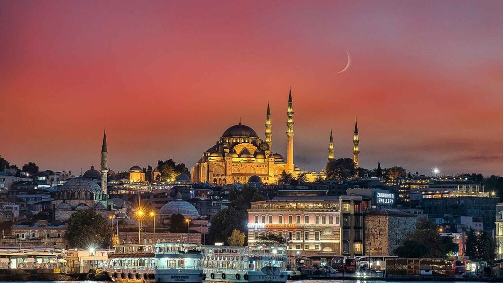 A cityscape at dusk with a prominent mosque featuring multiple minarets and domes, illuminated against a twilight sky. 5