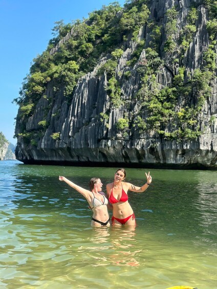 Two people in a clear body of water with rocky cliffs in the background. 4