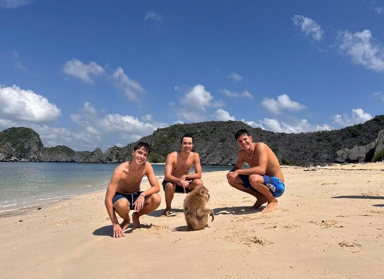 Three people on a sandy beach with a rocky coastline and clear blue sky. 1