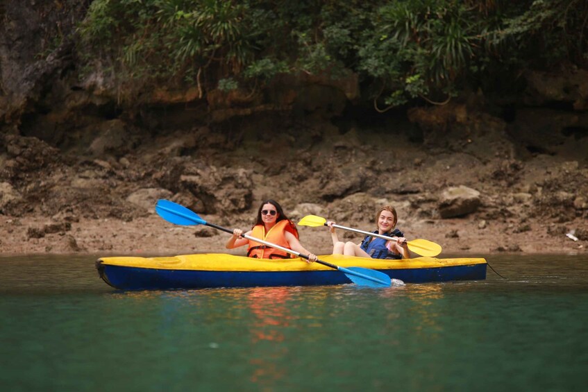 Two people kayaking on a river with a rocky riverbank and greenery in the background. 3