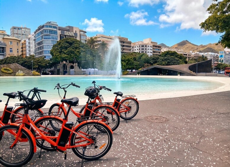 A fountain, bicycles, and buildings in a sunny urban setting. 2