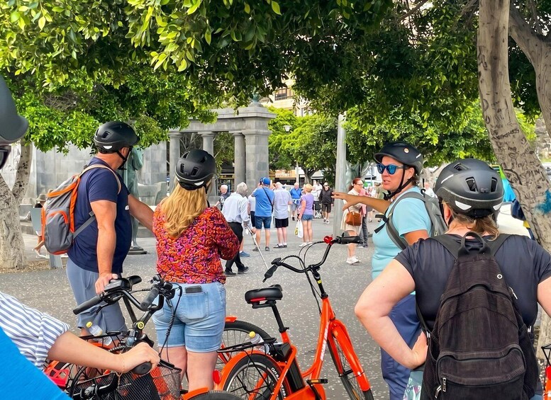 A group of people with bicycles, some wearing helmets, gathered around a monument in a park. 5