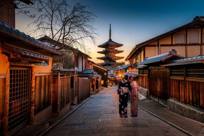 A traditional Japanese street with wooden buildings, a pagoda, and two people in kimono. 1