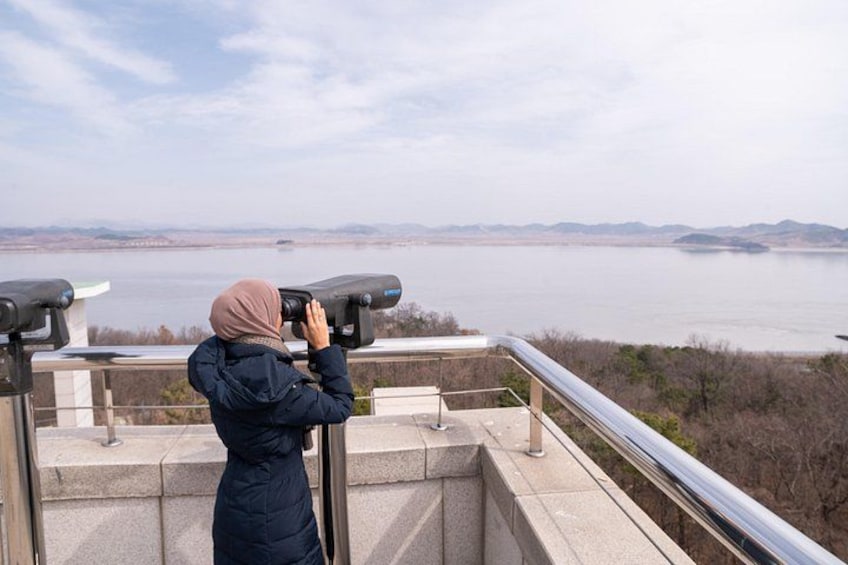 A person using binoculars overlooking a body of water with distant landforms. 2