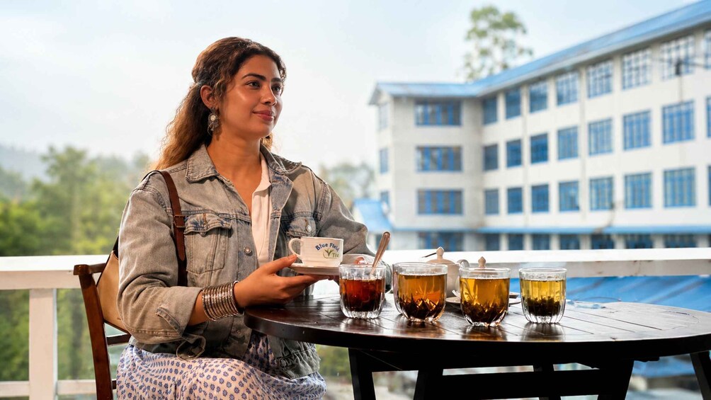 A person sitting at a table with a tray holding a cup labeled 'Blue Field Tea,' and several glasses of tea on the table. 4