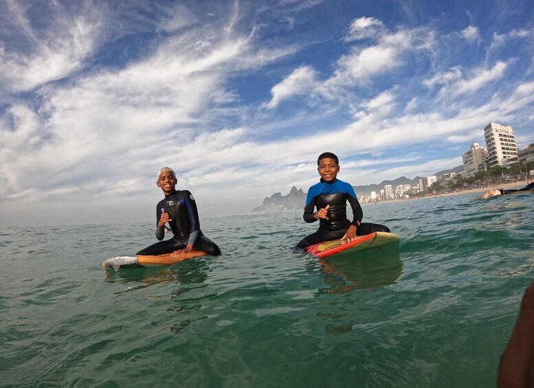 Two people sitting on surfboards in the ocean with a cityscape in the background. 2