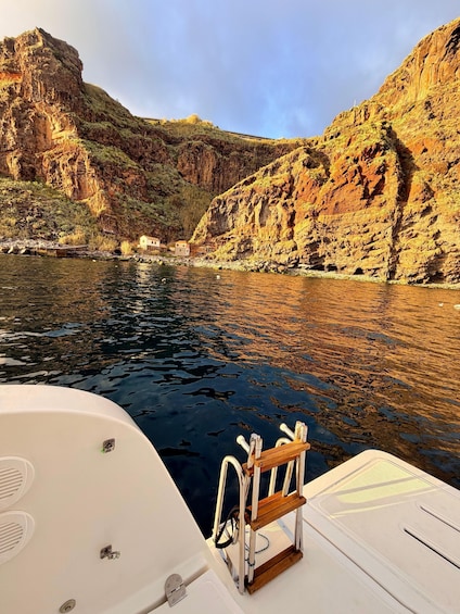 A boat's deck with a lifebuoy and metal railings, a calm river, rocky cliffs, and a small building on the shore. 5