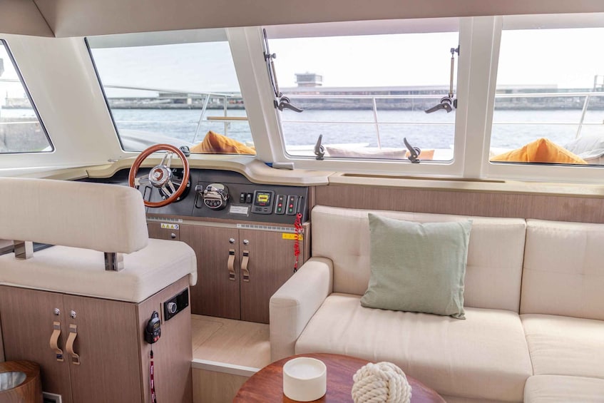 A boat interior with a steering wheel, control panel, cushioned seating, and a view of a bridge through the windows. 3