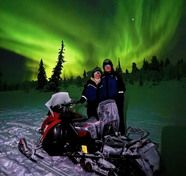 Two people on a snowmobile with the Northern Lights in the background. 1