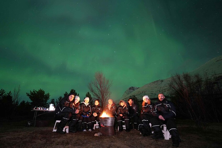 A group of people sitting around a campfire at night with the aurora borealis in the background. 4