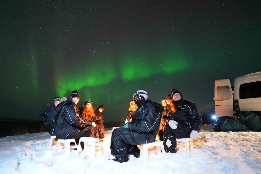 People sitting on stools under a night sky with the aurora borealis. 3