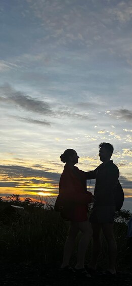Two people standing on a grassy hill with a sunset in the background. 1