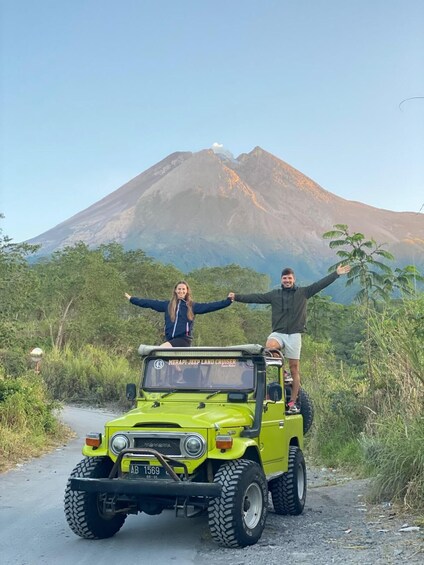 A green off-road vehicle with two people standing on top, a mountain in the background, and a clear sky. 2
