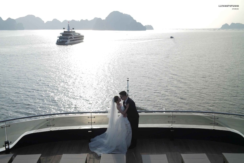 A couple kissing on a boat deck with a body of water and distant islands in the background. 3