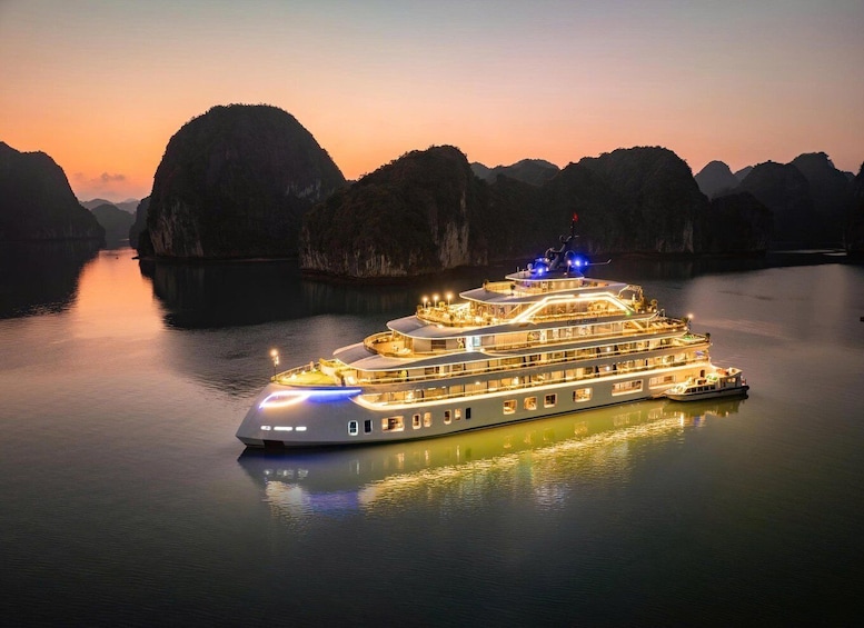 A large illuminated cruise ship at sunset with multiple decks and a docked tugboat. 1