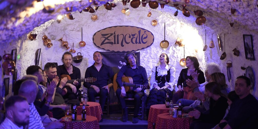 A group of people seated on stage with a sign reading 'Zincalé' in the background. 4