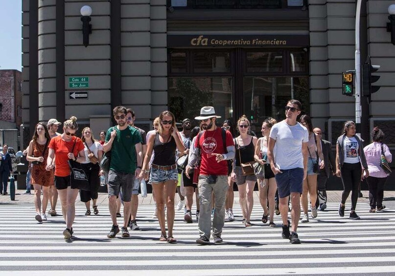 A group of people crossing a street at a crosswalk in front of a building with a sign that reads "Cooperativa Financiera". 4