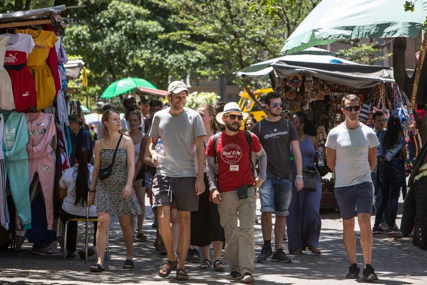 A busy outdoor market with people walking and various stalls selling clothes. 1