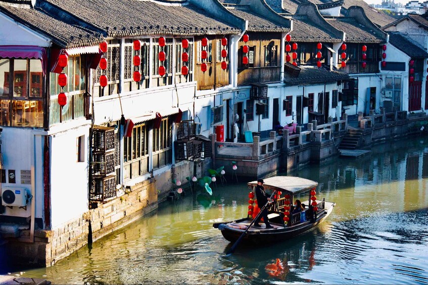 A traditional boat on a narrow waterway between old buildings adorned with red lanterns. 3