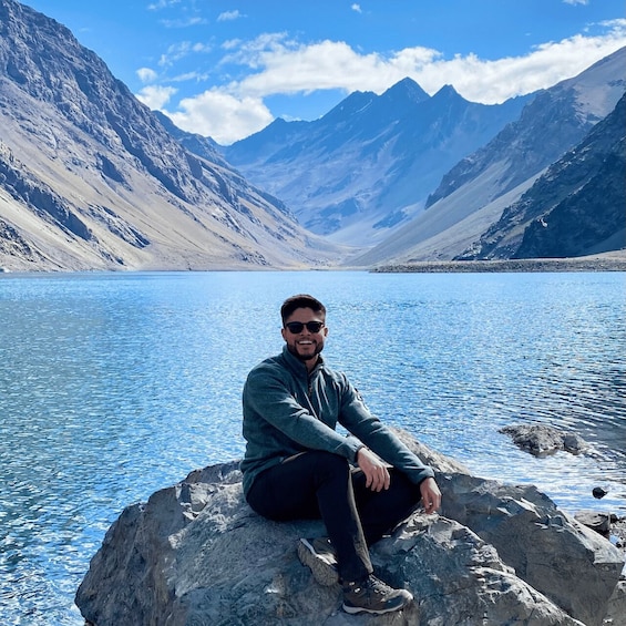 A person sitting on a rock by a lake with mountains in the background. 1