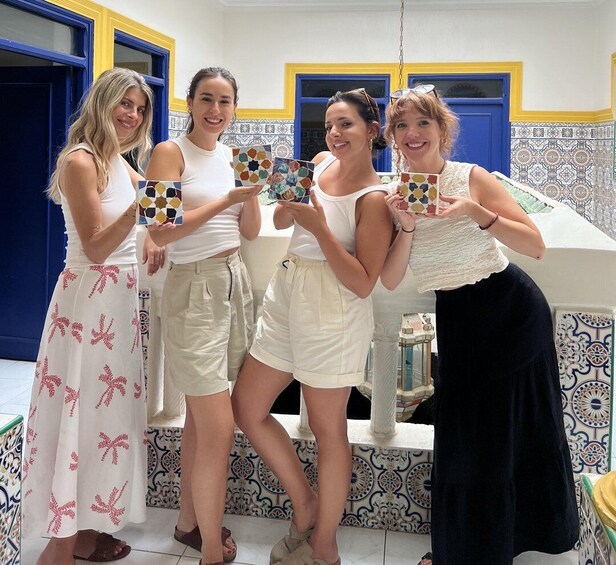 Four women holding colorful cards in a room with blue and yellow doors and patterned tiles. 1