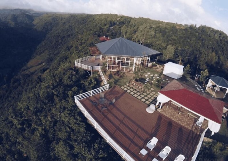 A large house with a wooden deck and a red roof, surrounded by a forested hillside. 3